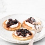 Three pancakes topped with crème fraiche and smashed blueberries