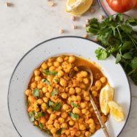 Plate with chickpea tomato curry with lemon wedge and spoon