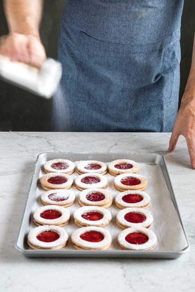 Sprinkling powdered suger over raspberry linzer cookies