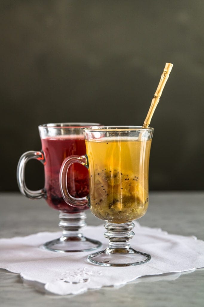 two glasses with roasted fruit tea. red glass mug with berry tea and yelllow/green with tropical variation