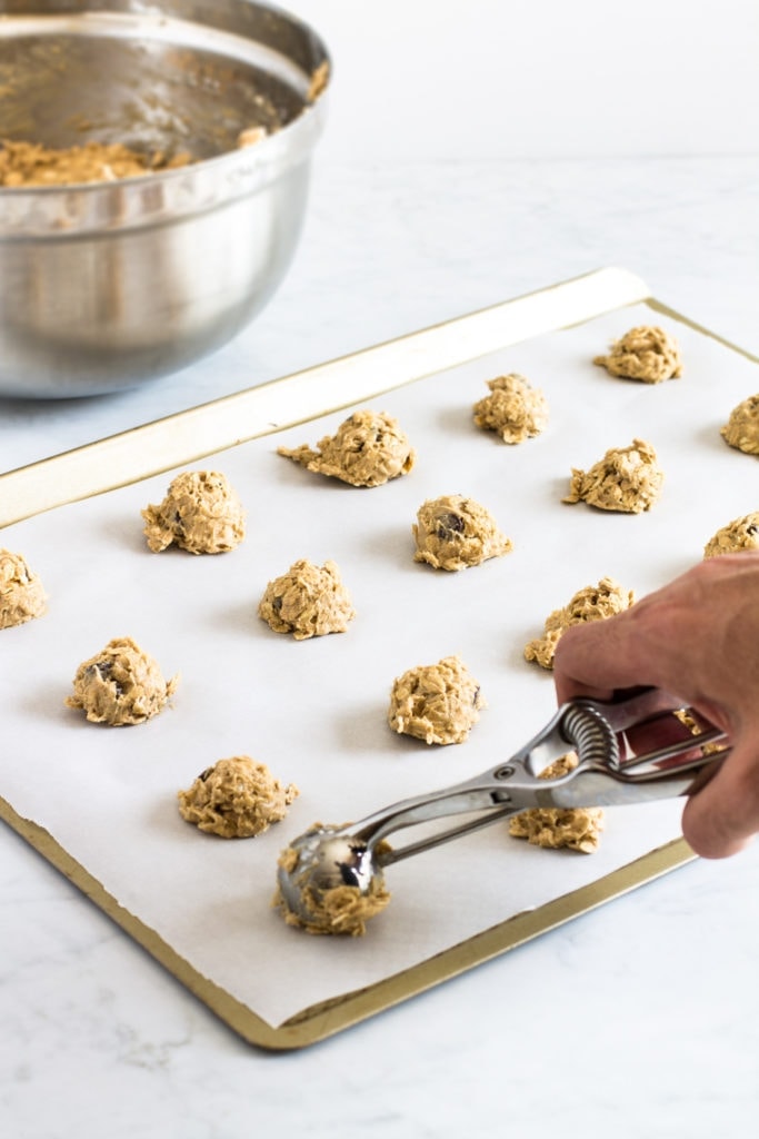 scooping out cookie dough on a baking sheet.