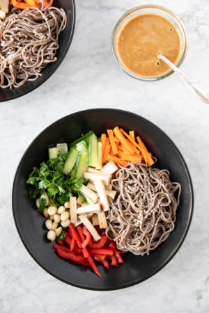 black bowl with soba noodle salad, with peanut butter dressing on the side