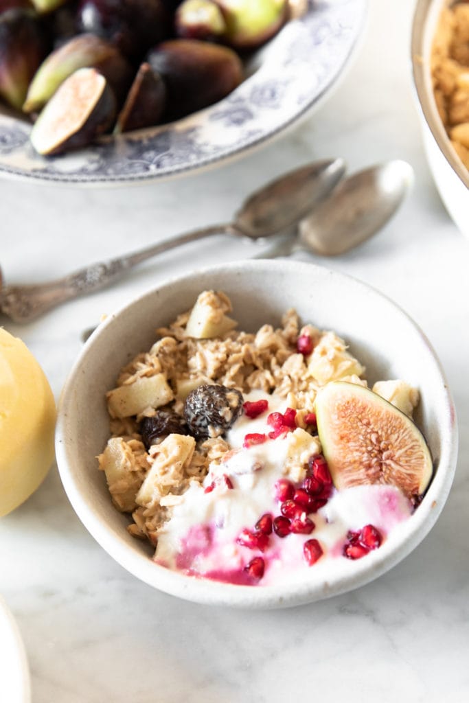 Bowls with Bircher Muesli (overnight oats), peeled apple, spoons, fresh figs, pomegranate seeds, and yogurt