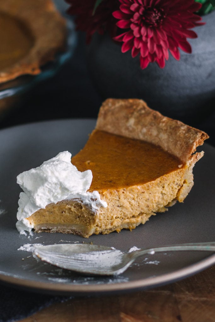 Slice of pumpkin pie with spelt crust, topped with whipped cream