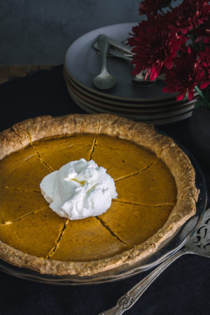 Sliced pumpkin pie with spelt crust, topped with whipped cream