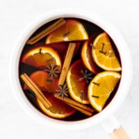 White saucepan with ingredients for mulled wine: red wine, cinnamon sticks, sliced orange, star anise and whole cloves
