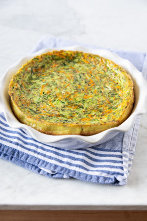 Crustless carrot zucchini quiche in a baking dish, on top of a blue/white kitchen towel