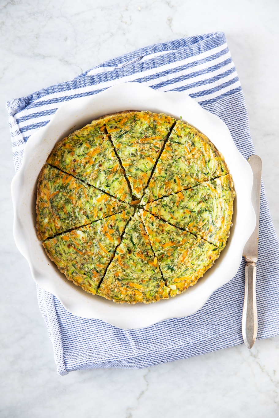 Crustless carrot zucchini quiche in a baking dish, on top of a blue/white kitchen towel