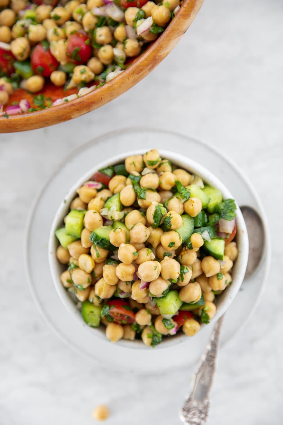 Small white bowl with Easy Chickpea Salad With Tomatoes and Cucumbers and silver spoon